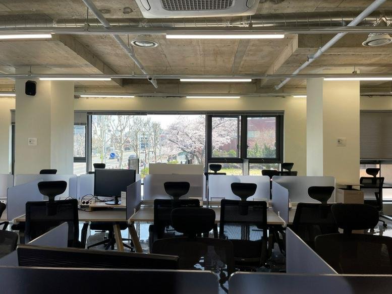 Spacious open-plan workspace at Dowon Hall with rows of desks and large windows overlooking trees.