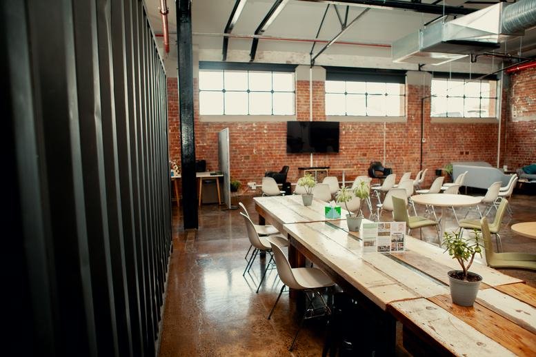 Large industrial coworking space with long wooden tables and exposed brickwork.