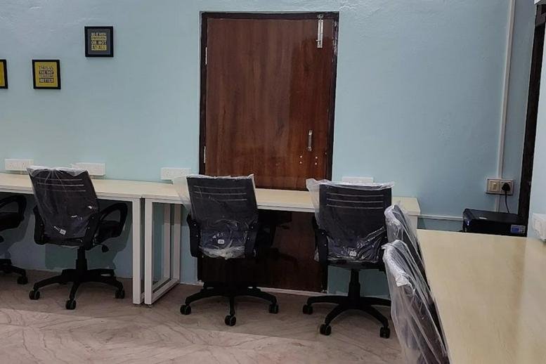 Workspace at 35, Gangadeeshwar Koil Street, Chennai featuring wooden desks and black mesh chairs against a pale blue wall.