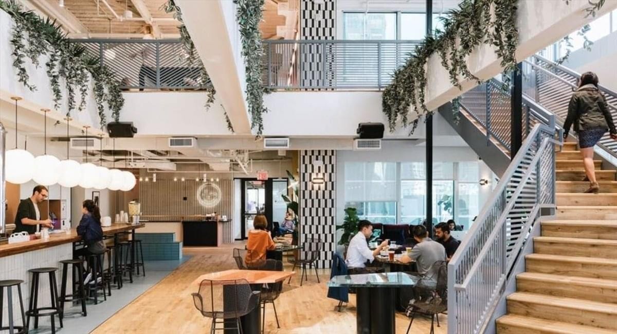 Spacious communal lounge and cafe at Global Gate Nagoya with high ceilings, plants, and a wooden staircase.