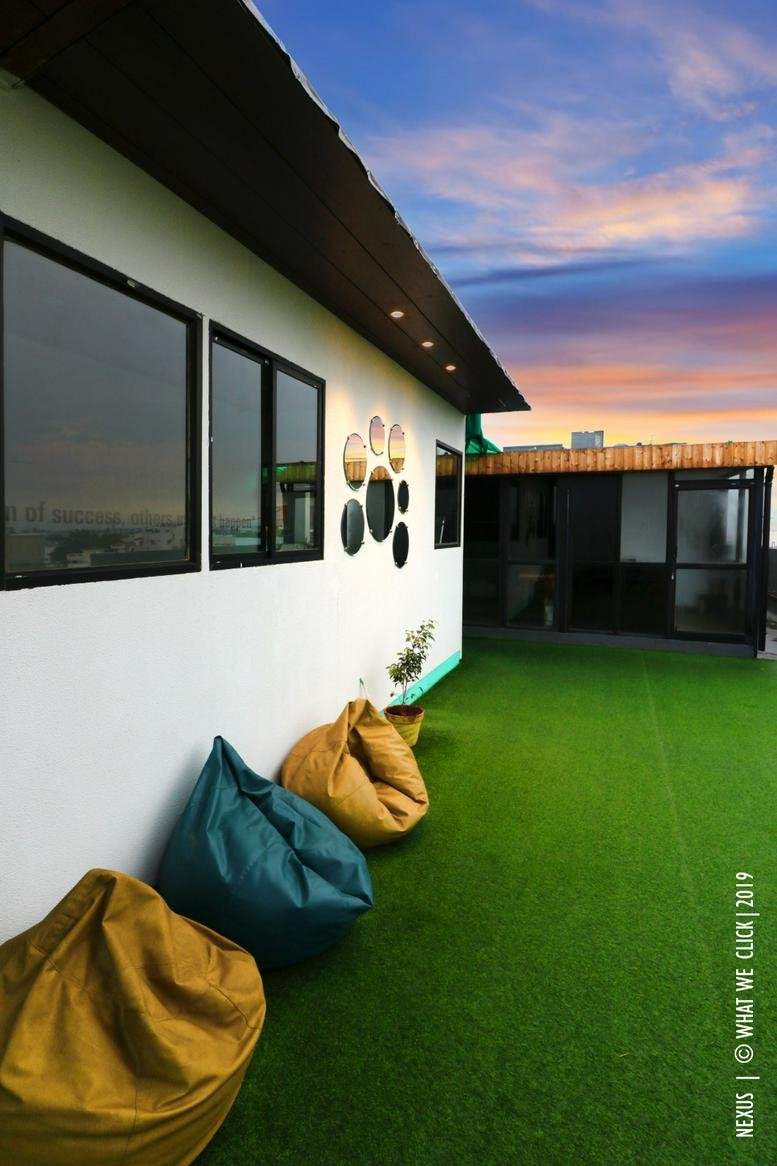 Exterior rooftop terrace at Nexus Spaces, Vishal Astra with bean bags and artificial grass under a sunset sky.