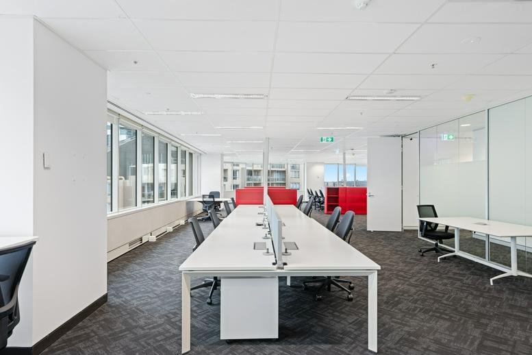 Open-plan coworking space with long white desks and red privacy screens.