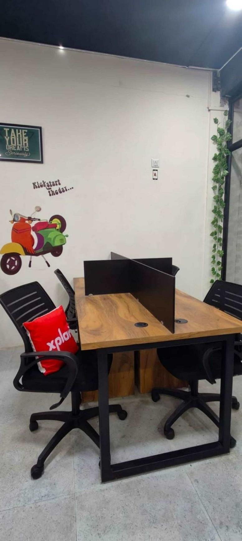 Workspaces at Bajpai Sons Building with wooden desks, black chairs, and a colorful wall mural.