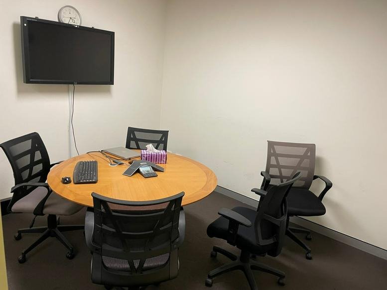 Meeting room at 61 Market Street with a round wooden table, four mesh chairs, and a wall-mounted TV.