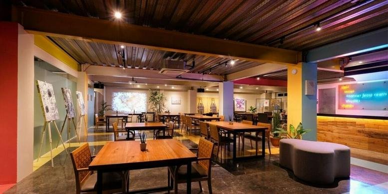 Spacious communal lounge at Building 4, JDN Square with wooden tables, warm lighting, and a modern industrial ceiling.