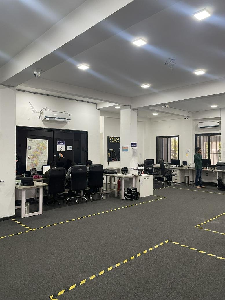 Spacious open-plan office area with workstations and yellow-striped floor markings.