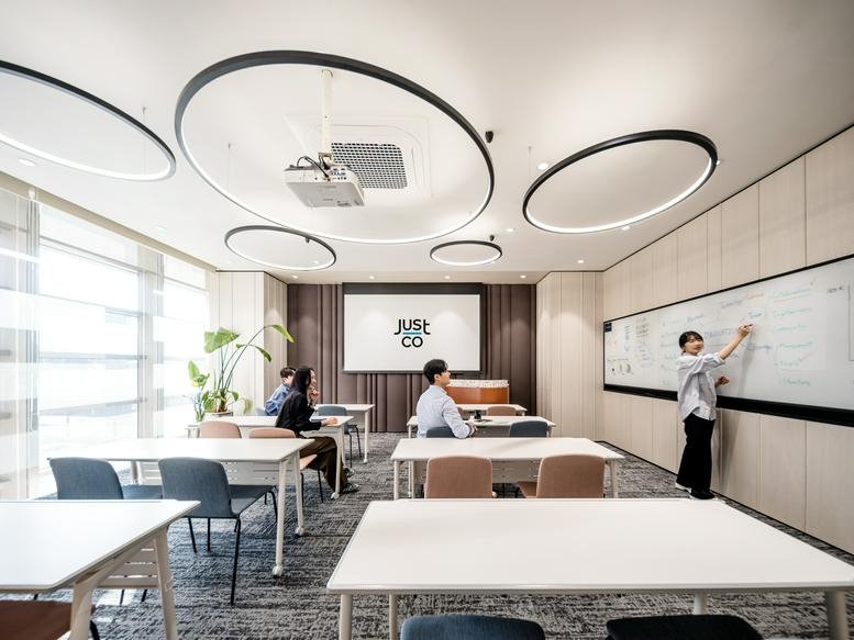 Bright training room with white tables, colorful chairs, and a person writing on a large whiteboard.