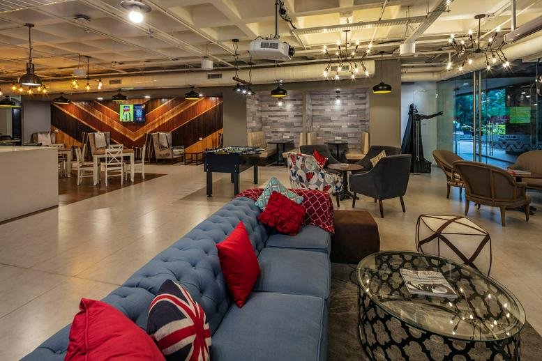 Communal lounge area with a blue tufted sofa, red pillows, and a Union Jack cushion.