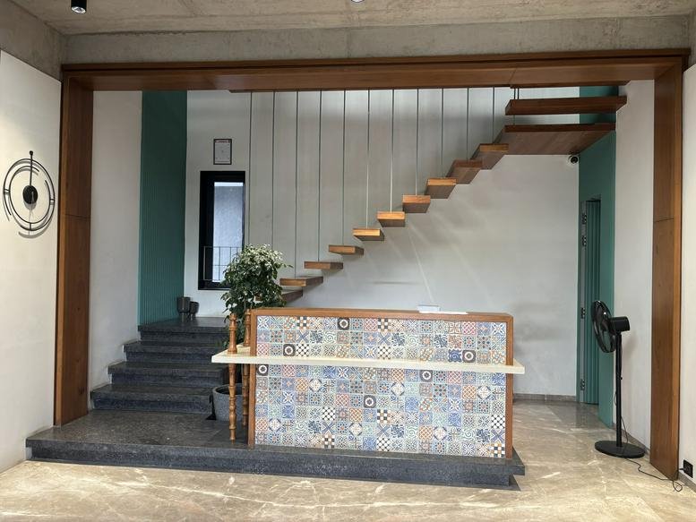 Modern reception area at Dange Chowk Road, Pimpri-Chinchwad featuring a tiled desk and floating wooden stairs.