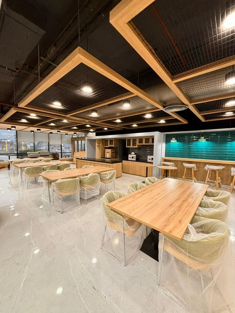 Spacious communal cafeteria and lounge area with wooden tables, bar seating, and warm overhead lighting.