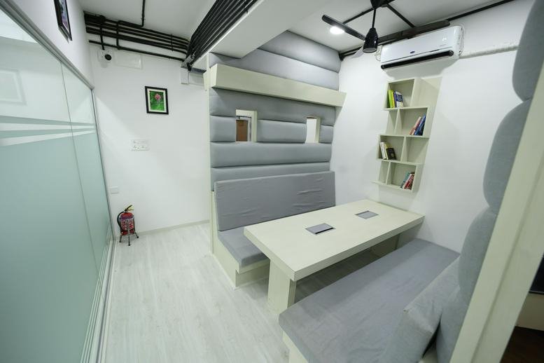 A comfortable breakout booth with padded grey walls and a white table at Gee Plaza.