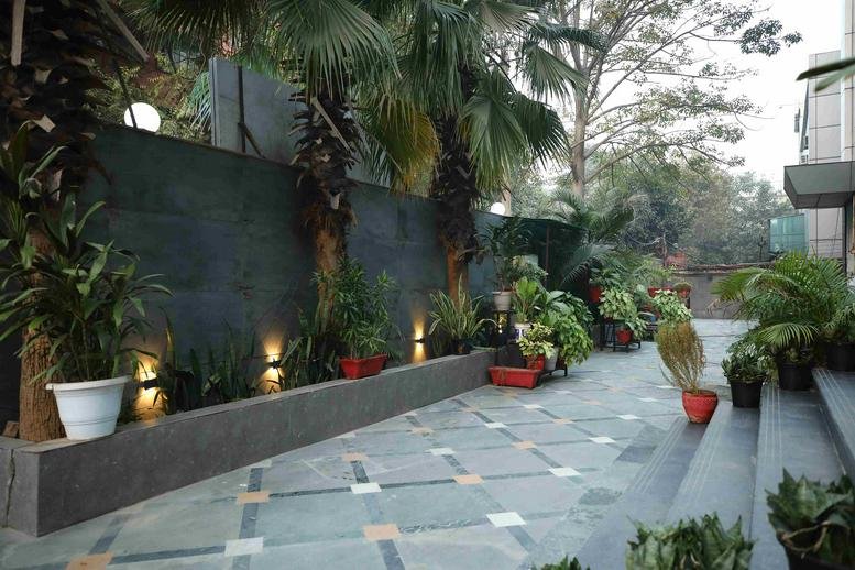 Exterior entrance area of FB-B1 Extension, First Floor, Mohan Estate, New Delhi with stone tiling and palm trees.