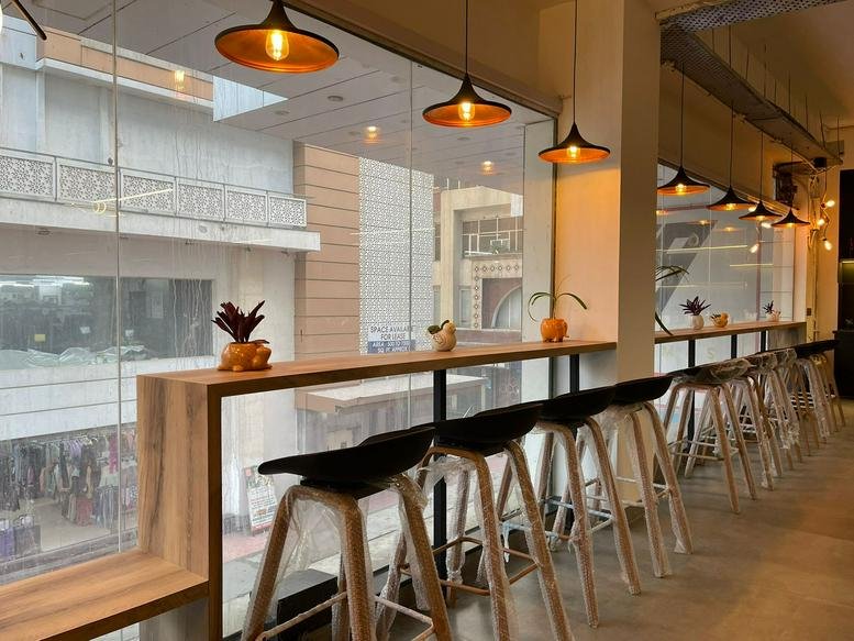 Spacious communal lounge at Garg Trade Centre with bar seating, wooden accents, and hanging pendant lights.