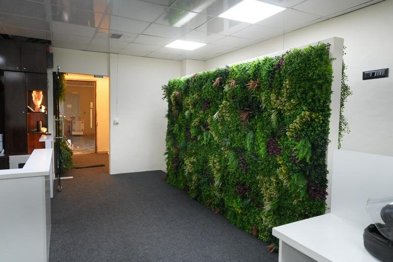 Reception area at Janta Market Road, Navi Mumbai featuring a lush green artificial plant wall and white desk.
