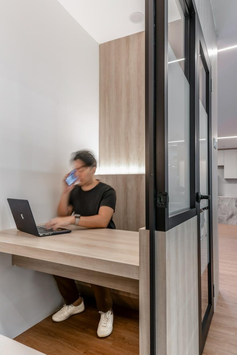 A person working at a laptop in a private glass-enclosed phone booth.