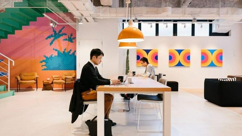 Bright coworking space at KDX Toranomon featuring a large communal table and vibrant wall murals.