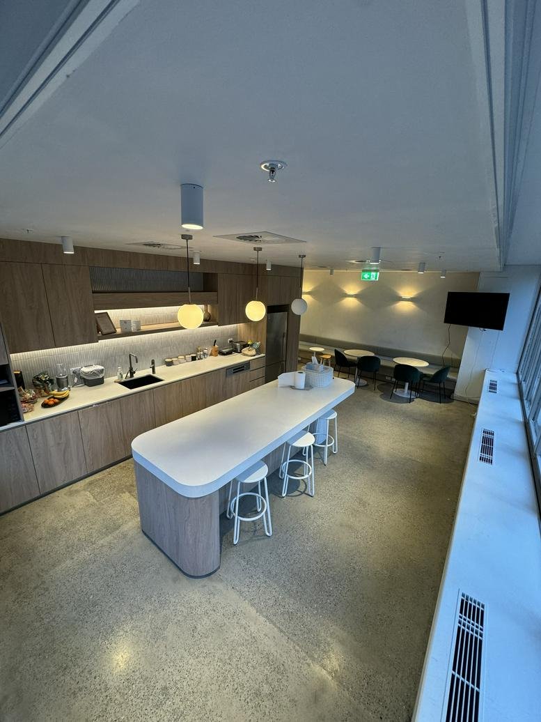 Wide-angle view of a modern kitchen and breakout area with wooden cabinetry and a long island.