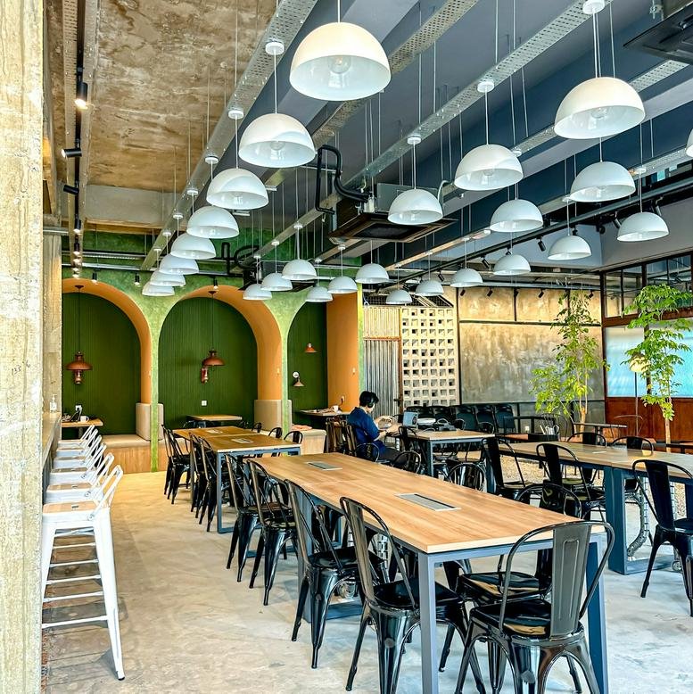 Communal coworking area at Lot 10 Jalan PJS 11/18 with arched green walls, wooden tables, and hanging dome lights.