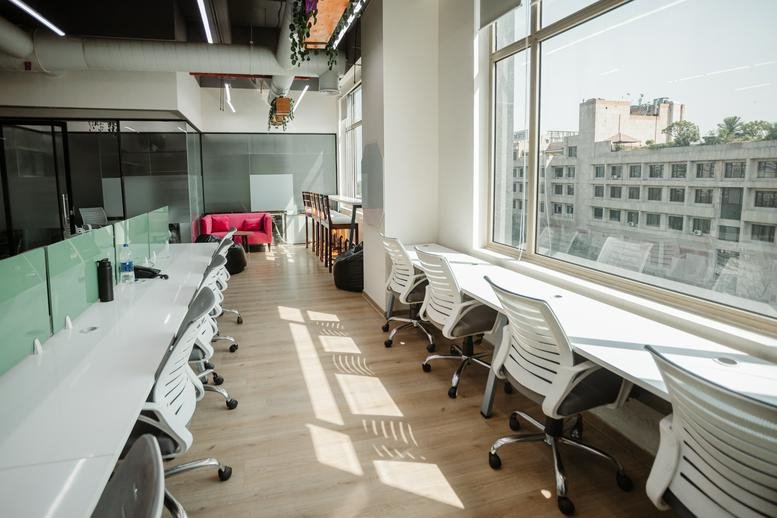 Bright open-plan workspace at JMD Empire Square with long white desks and large windows overlooking the city.