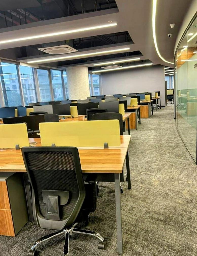 Spacious open-plan workspace at Neco Garden Road, Pune, India with wooden desks and yellow privacy dividers.