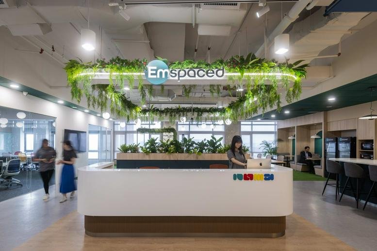 Bright, modern lobby at NU Tower 1 featuring a white reception desk, indoor plants, and overhead greenery.
