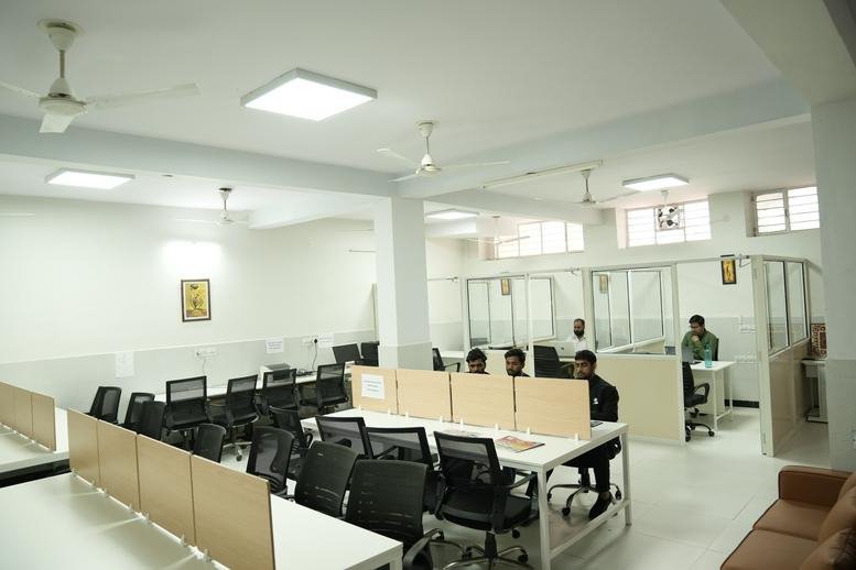 Spacious open-plan workspace with multiple rows of white desks and black ergonomic chairs.