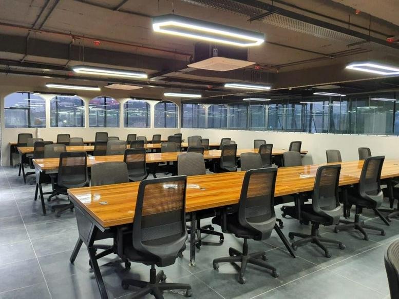 Spacious open-plan workspace at Plot Number 5, Survey Number 62, HITEC City, featuring wooden desks and mesh chairs.