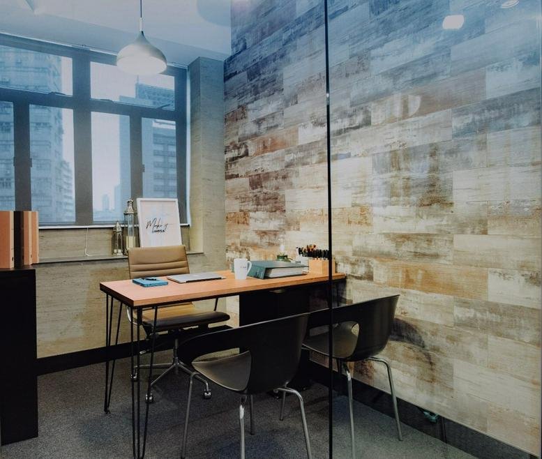 Private office at Riley House, Room 904 with a rustic wood wall and city views through large windows.