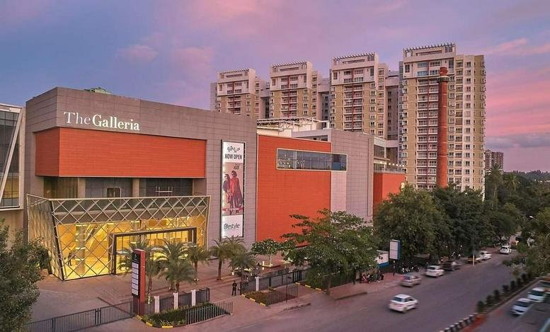 Exterior view of the contemporary RMZ Galleria building facade at sunset with integrated shopping and office spaces.