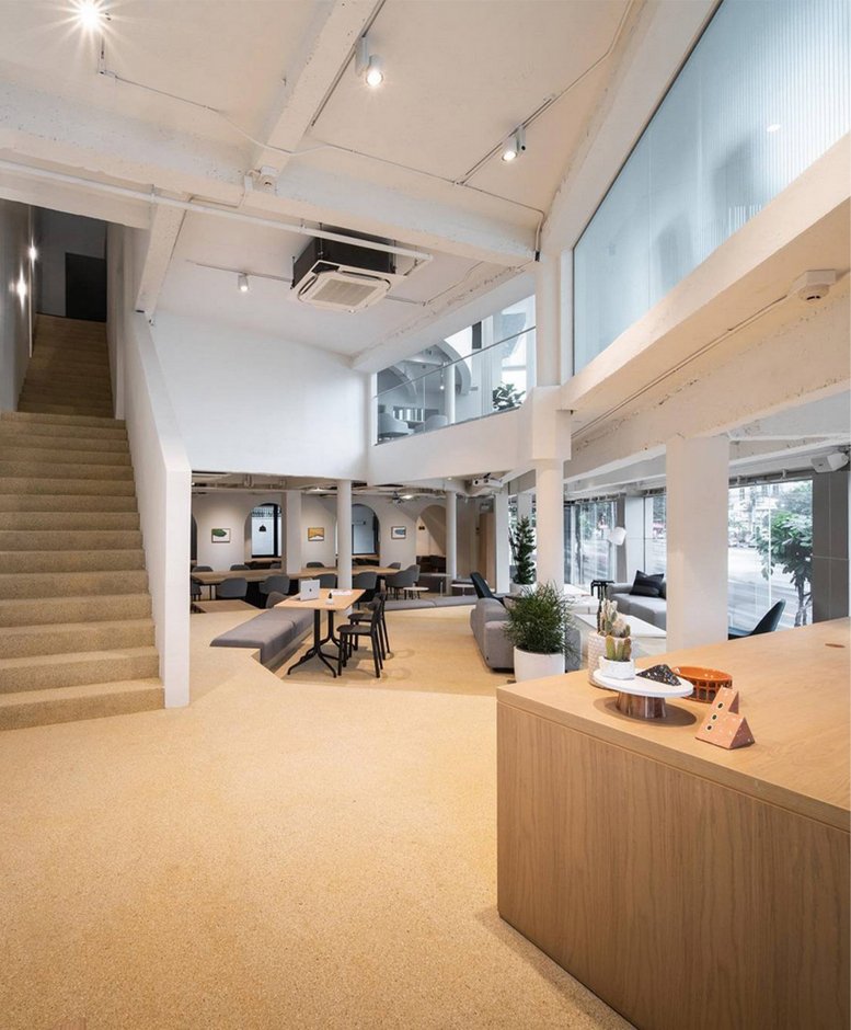 Spacious, double-height communal lounge with a staircase and warm lighting at 18 Ratchadaphisek Road.