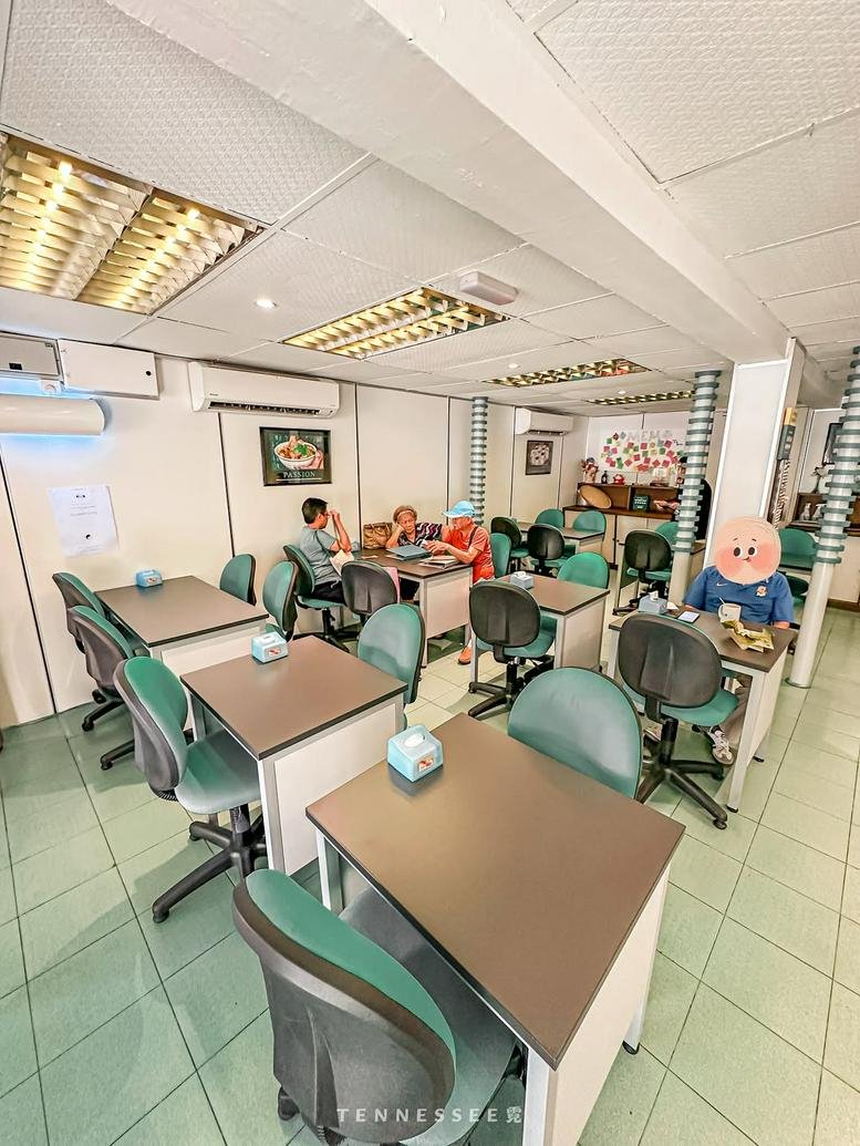 Spacious open-plan office layout with multiple green chairs and small work desks.