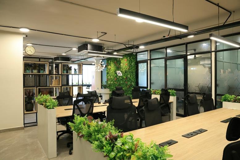 Spacious interior of Worklush Spaces with modern wooden desks, ergonomic chairs, and a lush green plant wall.
