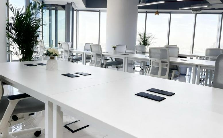Bright coworking area at Addax Tower featuring white desks, ergonomic chairs, and floor-to-ceiling windows.