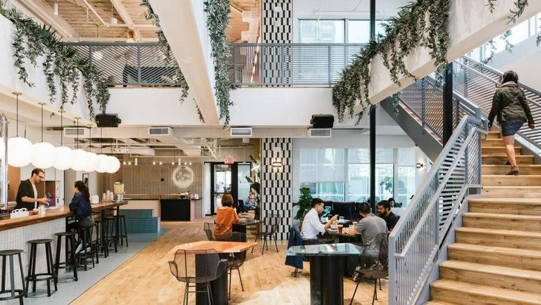 Spacious two-story communal atrium at 6 Gao Shan Nan Yi Street with hanging plants, wooden stairs, and café seating.