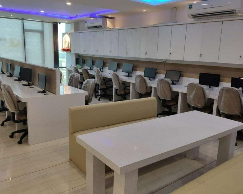 Spacious open-plan coworking area at Atulya IT Park featuring rows of computer workstations and a central white table.