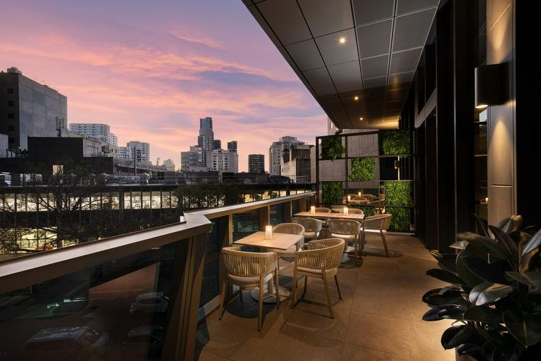 Outdoor terrace lounge with seating and city skyline views under a sunset sky.
