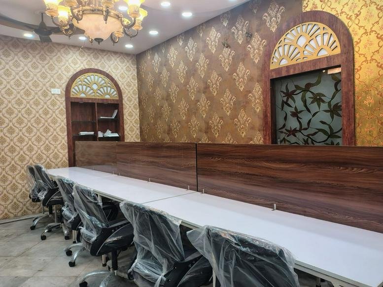 Open-plan coworking space at 68-A, Sadananda Road, Anami Sangha with long white desks and ornate patterned wallpaper.