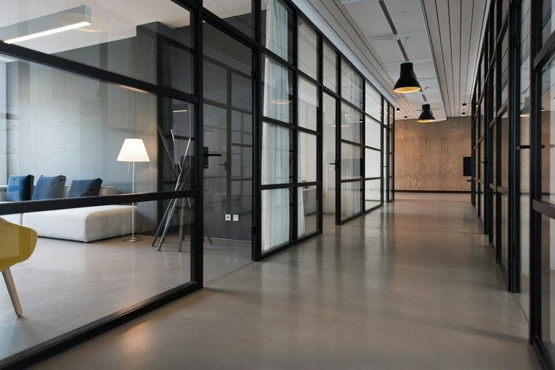 Modern corridor with black-framed glass partitions and industrial lighting.