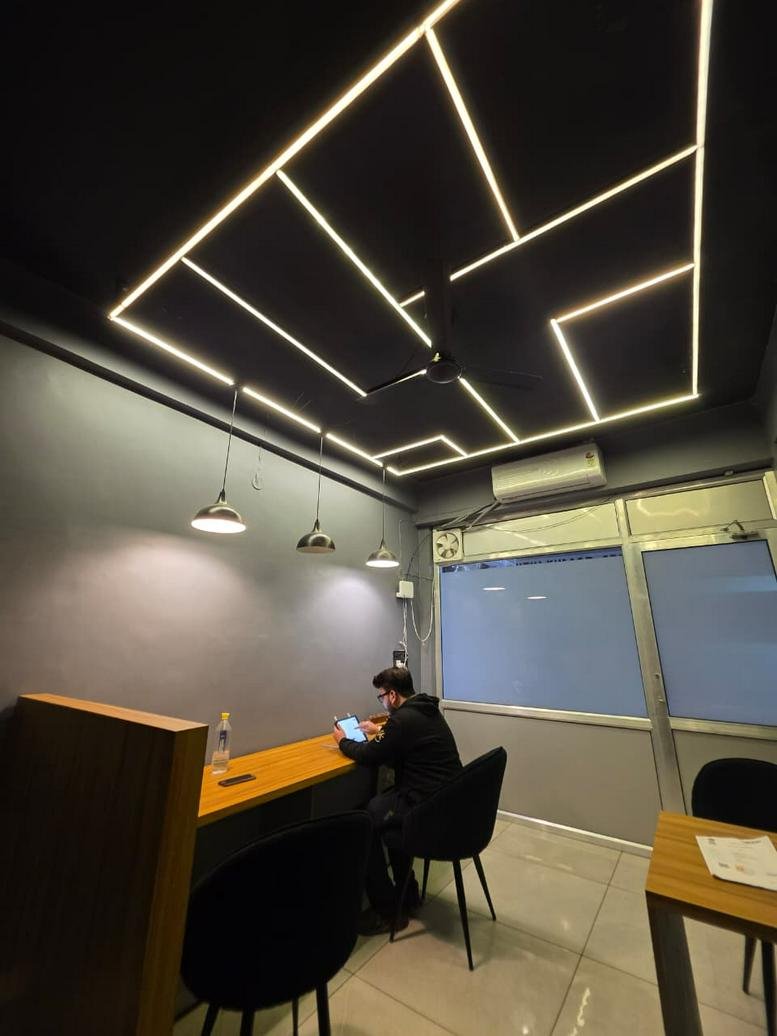 Workspace at BlackStation, Shivalik Complex with striking geometric LED ceiling lights and modern grey walls.