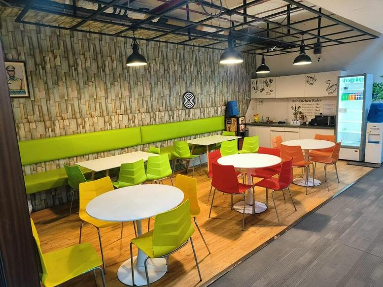 Vibrant communal dining area at Geek Space Business Centre with green benches and colorful chairs.