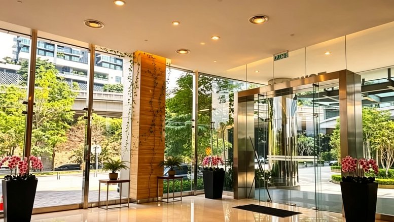 Spacious building lobby with polished floors, glass entrance doors, and decorative orchids.