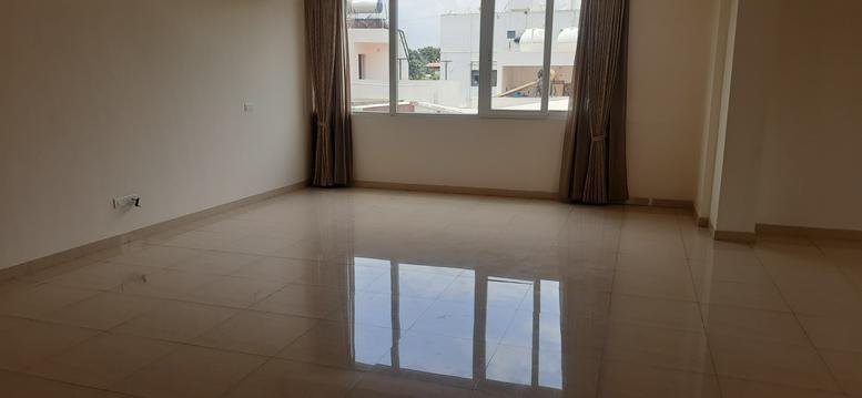 Spacious main hall at Nanda Gokulam with polished tile flooring and natural light from a window.