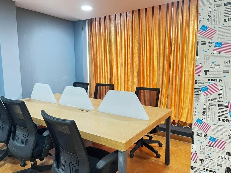 Meeting room at Sheeba’s Arcade featuring a wooden table, black chairs, and bright orange curtains.