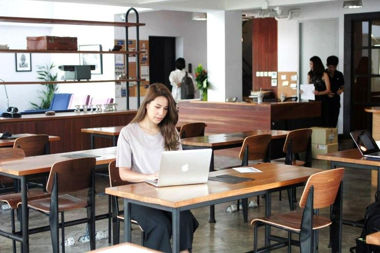 Spacious communal coworking lounge at The Hive Thonglor with wooden tables and professional seating.