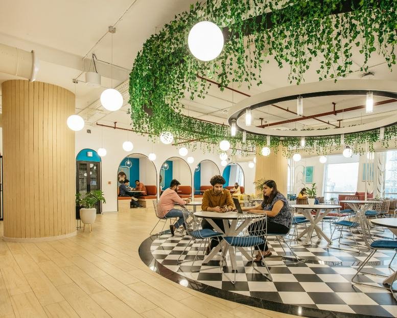 Spacious coworking area with hanging greenery and circular lighting.