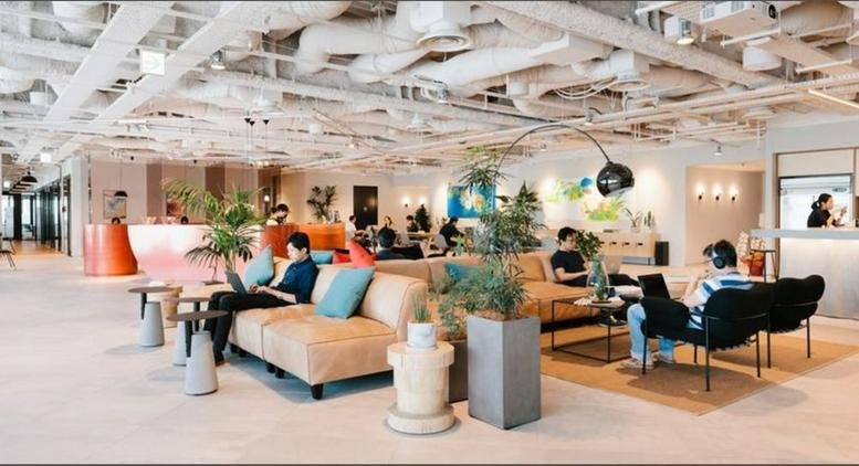 Spacious lounge at WeWork Metropolitan Plaza Building with eclectic seating, plants, and exposed ceiling.