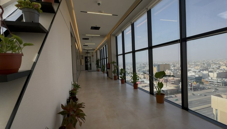 Luminous hallway at Custodian of The Two Holy Mosques Road with floor-to-ceiling windows and potted plants.