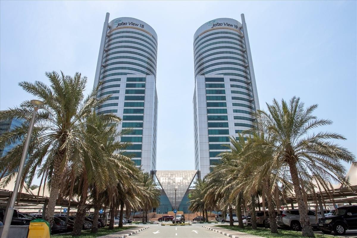 Exterior view of the twin tower complex at Jebel Ali, Free zone, Dubai, UAE surrounded by palm trees.