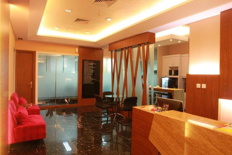 Warm, modern reception area at Kirana 2 Tower with a wooden front desk and plush red sofa.