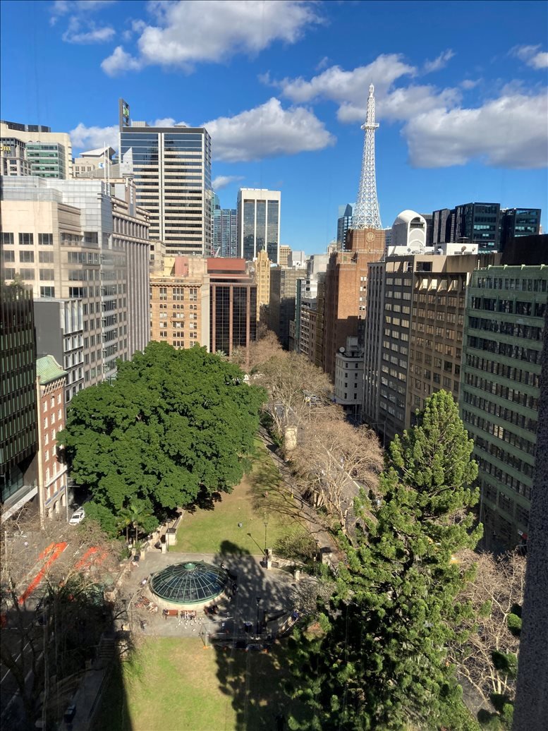 Aerial view of a city street with green park and tall buildings, clear sky.